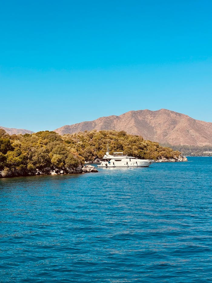 A luxury yacht cruising near a scenic island with mountains in the background.